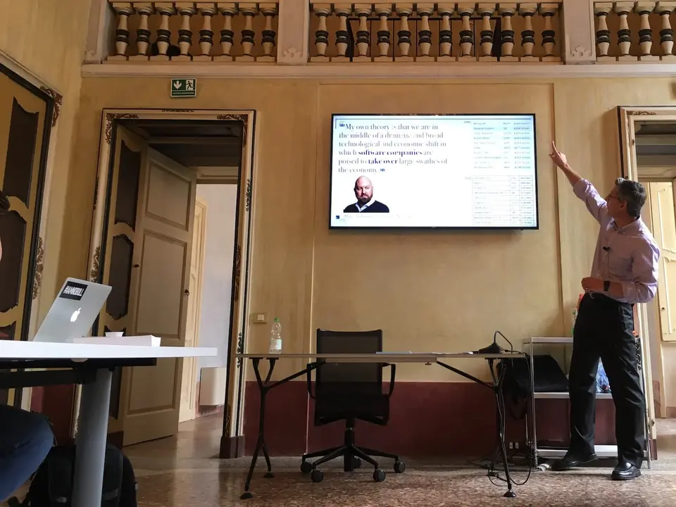 Un docente indica lo schermo durante una lezione in una sala storica con le pareti decorate