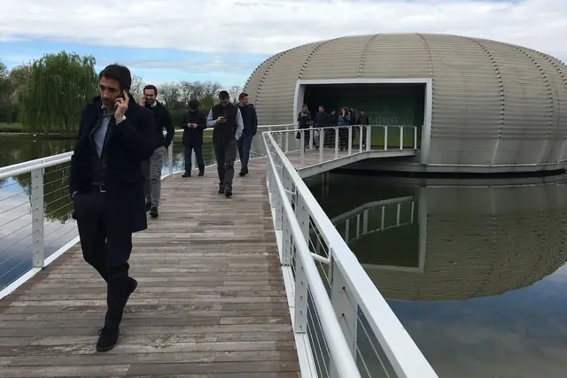 Un gruppo di corsisti attraversa una passerella sull'acqua verso un padiglione dalle forme arrotondate